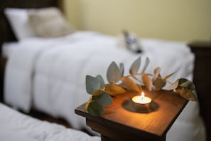 A wooden bedside table with a lit candle and eucalyptus leaves.