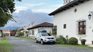 A gravel road leading to a white building with a tiled roof, a parked car, and a small garden area. - Sabor&arte (Antigua Guatemala)