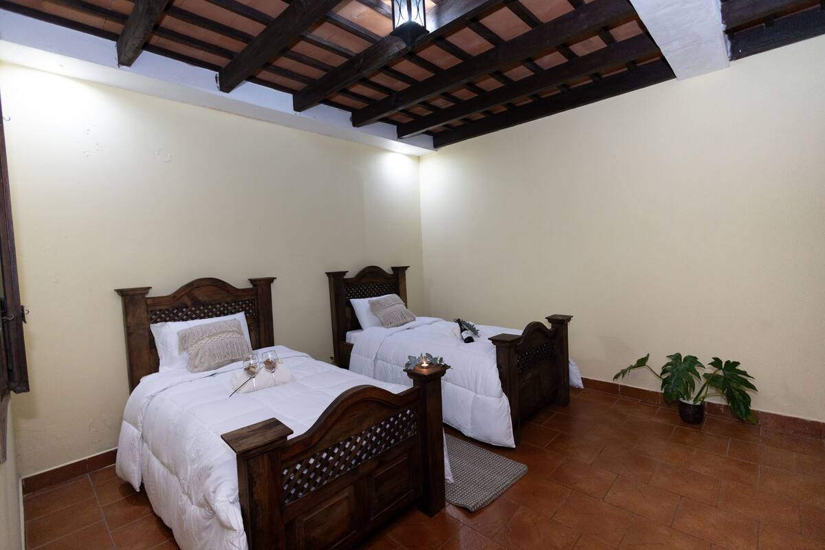 Une chambre à coucher avec deux lits en bois, un sol carrelé et un plafond avec des poutres apparentes.