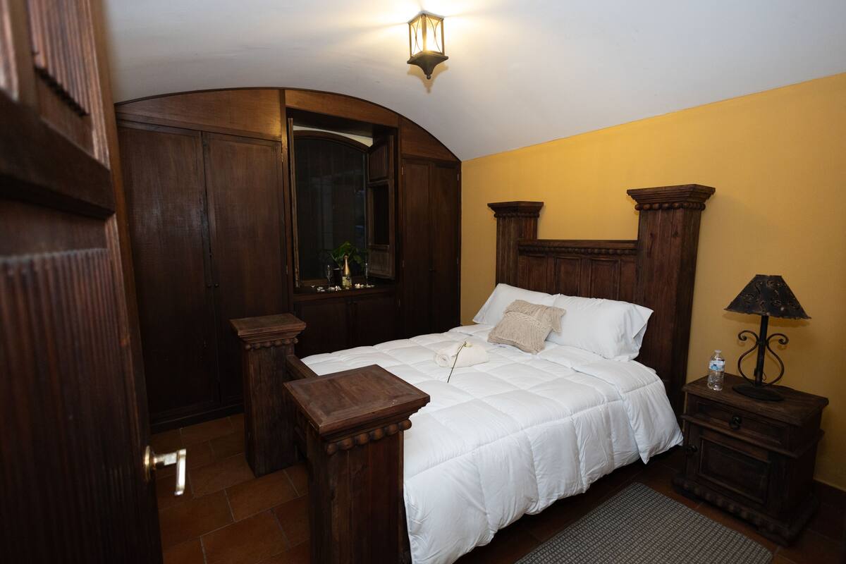 Une chambre à coucher avec un grand lit, une tête de lit en bois, une table de chevet, une lampe et un miroir.