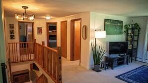 Una sala de estar con una escalera, un televisor, una planta y un cuadro en la pared.
