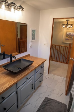 A bathroom with a wooden vanity, a black sink, and a mirror with light fixtures.