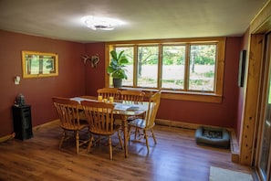 A dining area with a wooden table and chairs, a potted plant, and a window with a view of greenery.