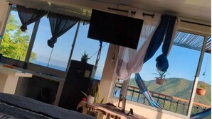 Una stanza con una grande finestra, una TV a schermo piatto, un'amaca e un tavolo con una pianta.