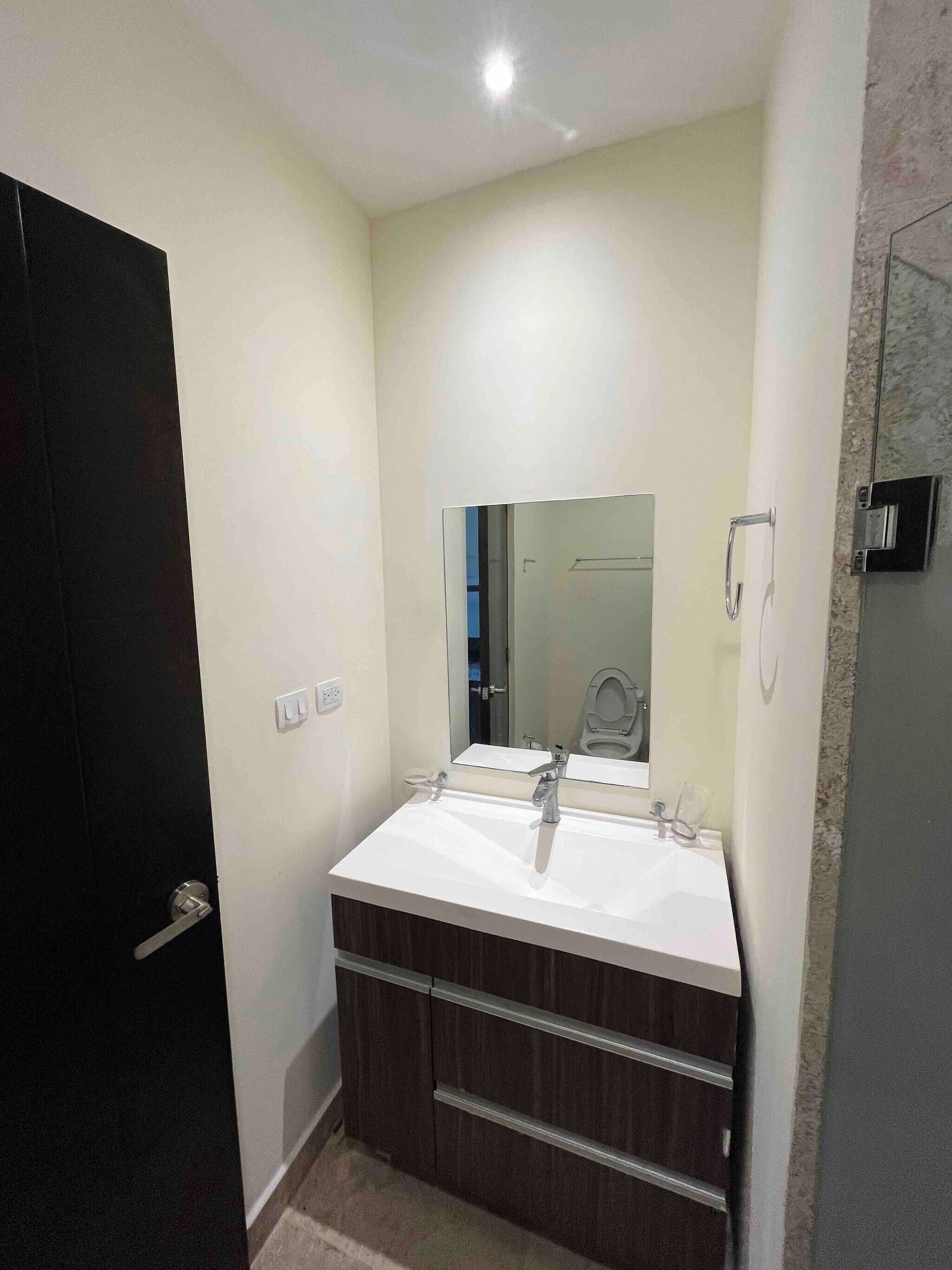 A bathroom with a white sink, dark wood vanity, a mirror, and a door.