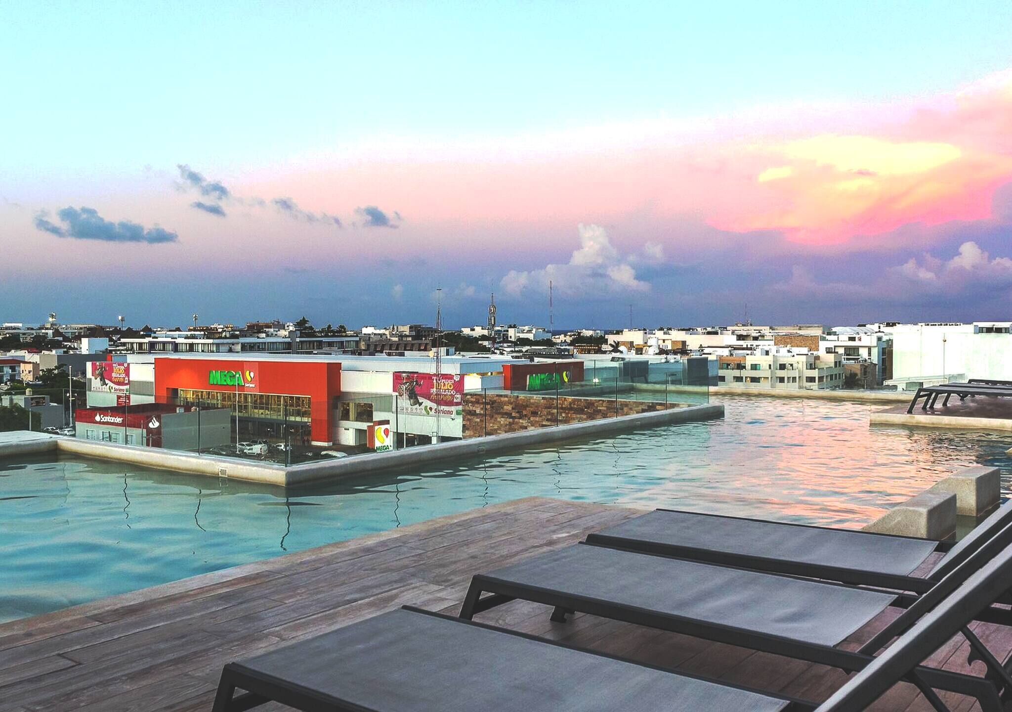 A rooftop pool with lounge chairs, a view of the cityscape, and a sunset sky.