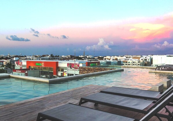 Une piscine sur le toit, agrémentée de chaises longues, offrant une vue sur le paysage urbain et un ciel au coucher du soleil.