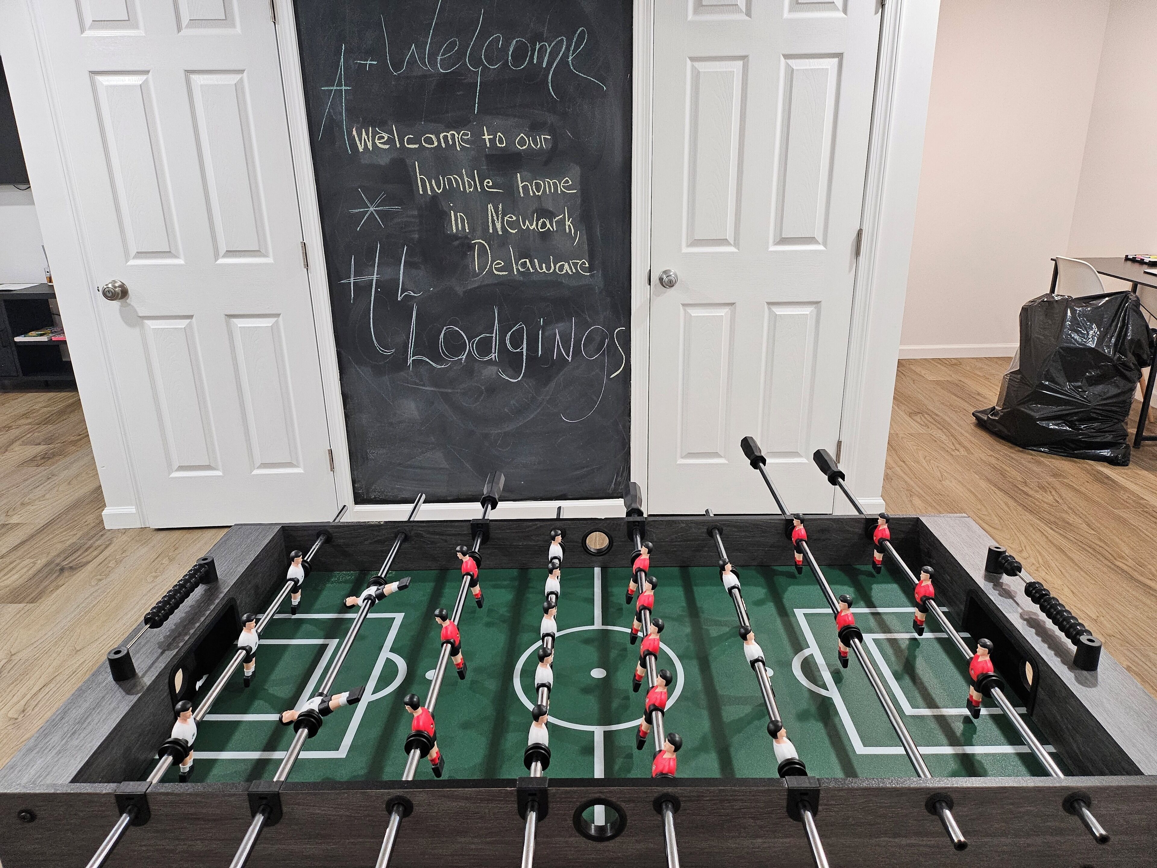 A foosball table with a chalkboard behind it displaying a welcome message.