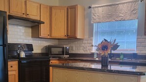 A kitchen with wooden cabinets, a microwave, a stove, and two bar stools. - Near University of Delaware, Christiana Care Hospital, & the Christiana Mall! (Newark)