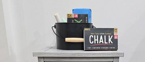 A rustic wooden nightstand with a chalkboard sign, a woven basket, and a black pot with writing utensils.