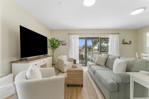 A modern living room with a flat-screen TV, two sofas, a coffee table, and a large window with curtains. - Classy Beachwood Villas Condo • Resort-Style Amenities • Quick Beach Access (Santa Rosa Beach)