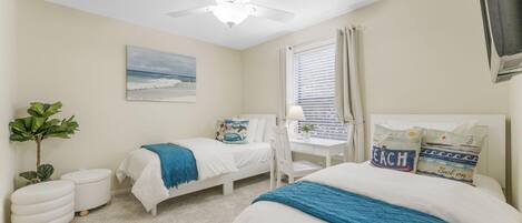 A bedroom with two beds, a ceiling fan, a desk with a chair, a window with blinds, and a plant.