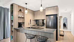 Una cocina moderna con armarios de madera, un refrigerador de acero inoxidable, una isla central con taburetes de bar, iluminación colgante y un espejo grande.