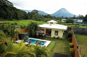 Une maison avec une piscine, entourée d’une végétation luxuriante et avec une montagne en toile de fond.