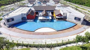 Una gran piscina envoltada d'edificis d'estil tropical, amb teulades de palla i una estructura central amb un rètol.
