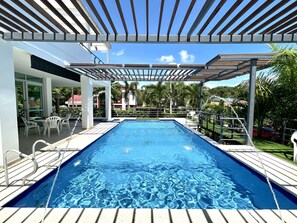 A swimming pool with a wooden deck and a pergola overhead.