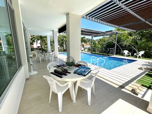 A poolside area with a table and chairs, a pool, and a view of the surrounding greenery.