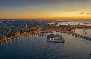A coastal cityscape at sunset with a marina, buildings, and a prominent tower. - All new, 100 sqm terrace & 5 min walk to the old town & shopping street (Bari)