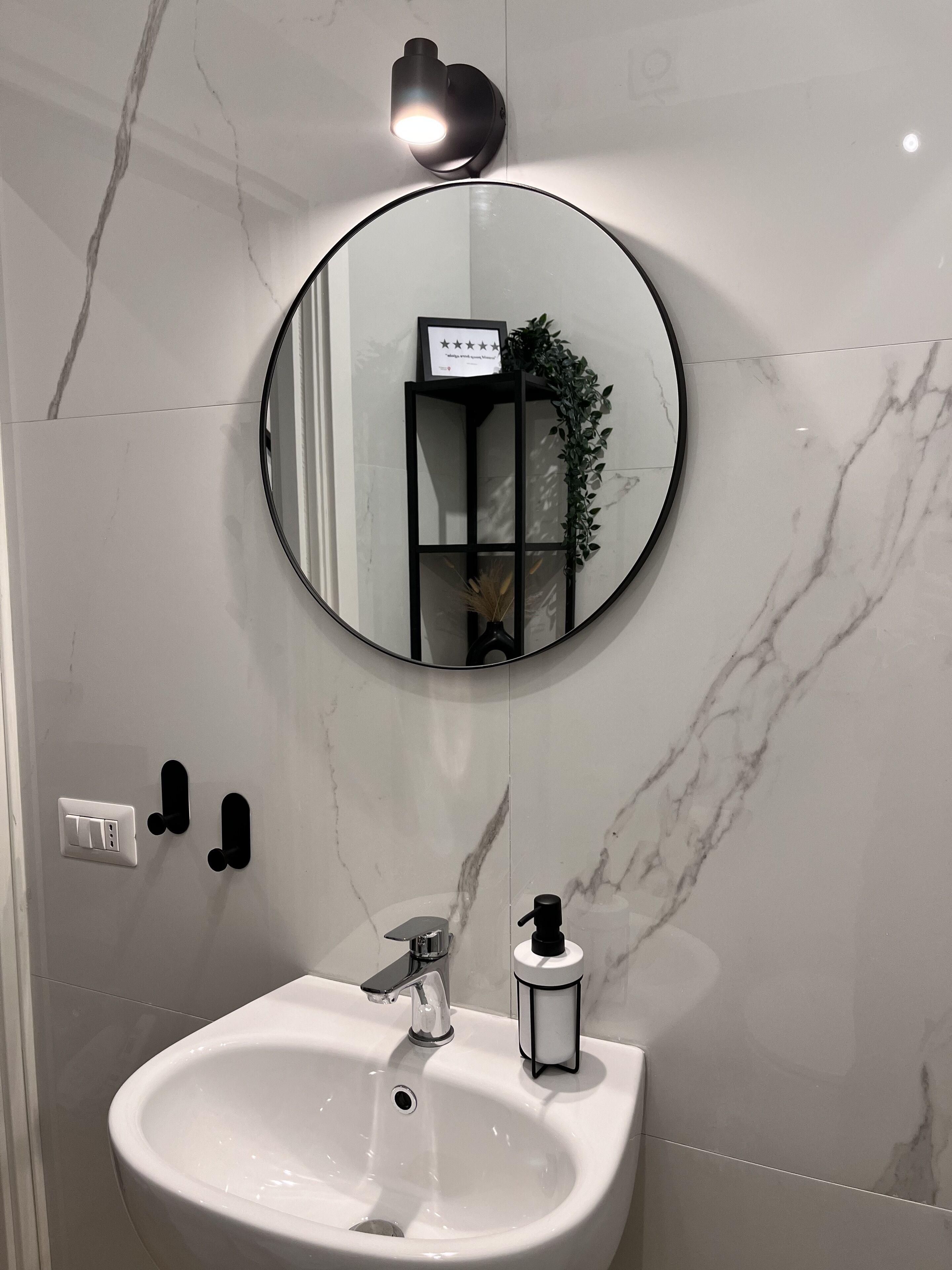 A bathroom with a white sink, a round mirror, and a wall-mounted light fixture.