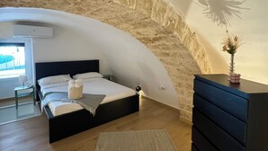 A bedroom with a curved stone wall, a bed, a dresser, and a small table with a lamp. - All new, 100 sqm terrace & 5 min walk to the old town & shopping street (Bari)