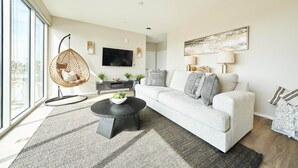 Un salon moderne avec un canapé, un fauteuil suspendu, une table basse et un téléviseur à écran plat.