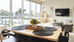 Un salon moderne avec une table à manger en bois, des sets de table noirs, un fauteuil suspendu et une grande fenêtre donnant sur la ville.