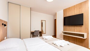 A hotel room with a bed, a desk, a chair, a mirror, a TV, and a shelf.