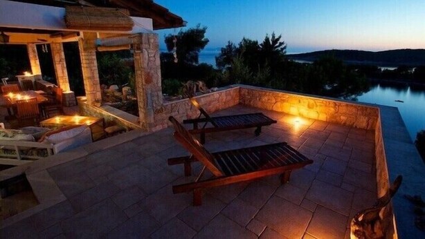 Una terraza en la azotea con suelo de piedra, dos sillones de madera y una mesa con sillas.