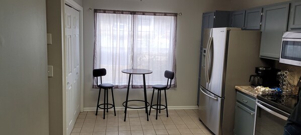 A compact kitchen with a refrigerator, microwave, and stove. There is a small dining area with two chairs and a table. - Ground floor Lake Martin Condo! (Dadeville)