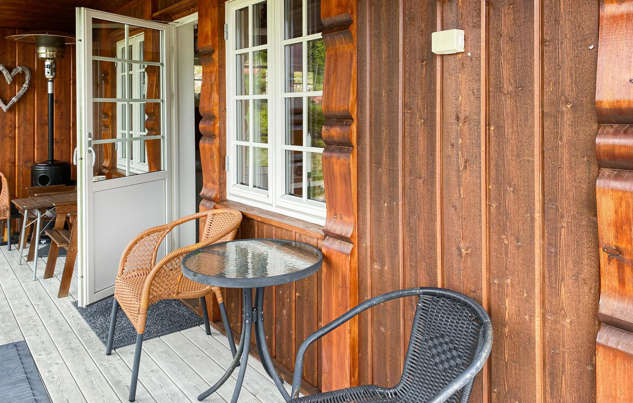 A wooden cabin with a glass door, two wicker chairs, a round table, and a small heater.