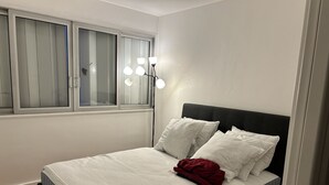 Una camera da letto con un letto, biancheria da letto bianca, una coperta rossa e una lampada da comodino.