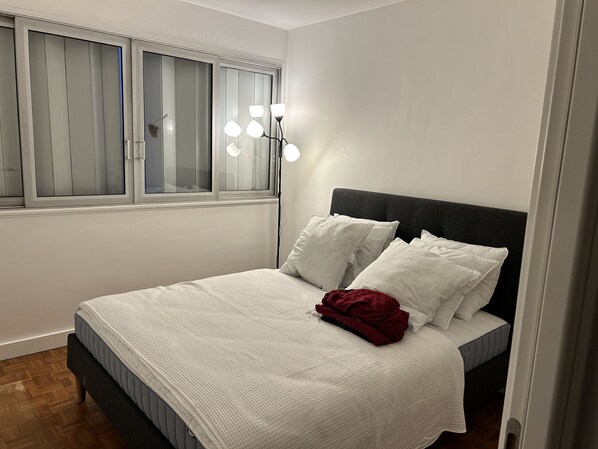 A bedroom with a bed, white bedding, a red blanket, and a bedside lamp.