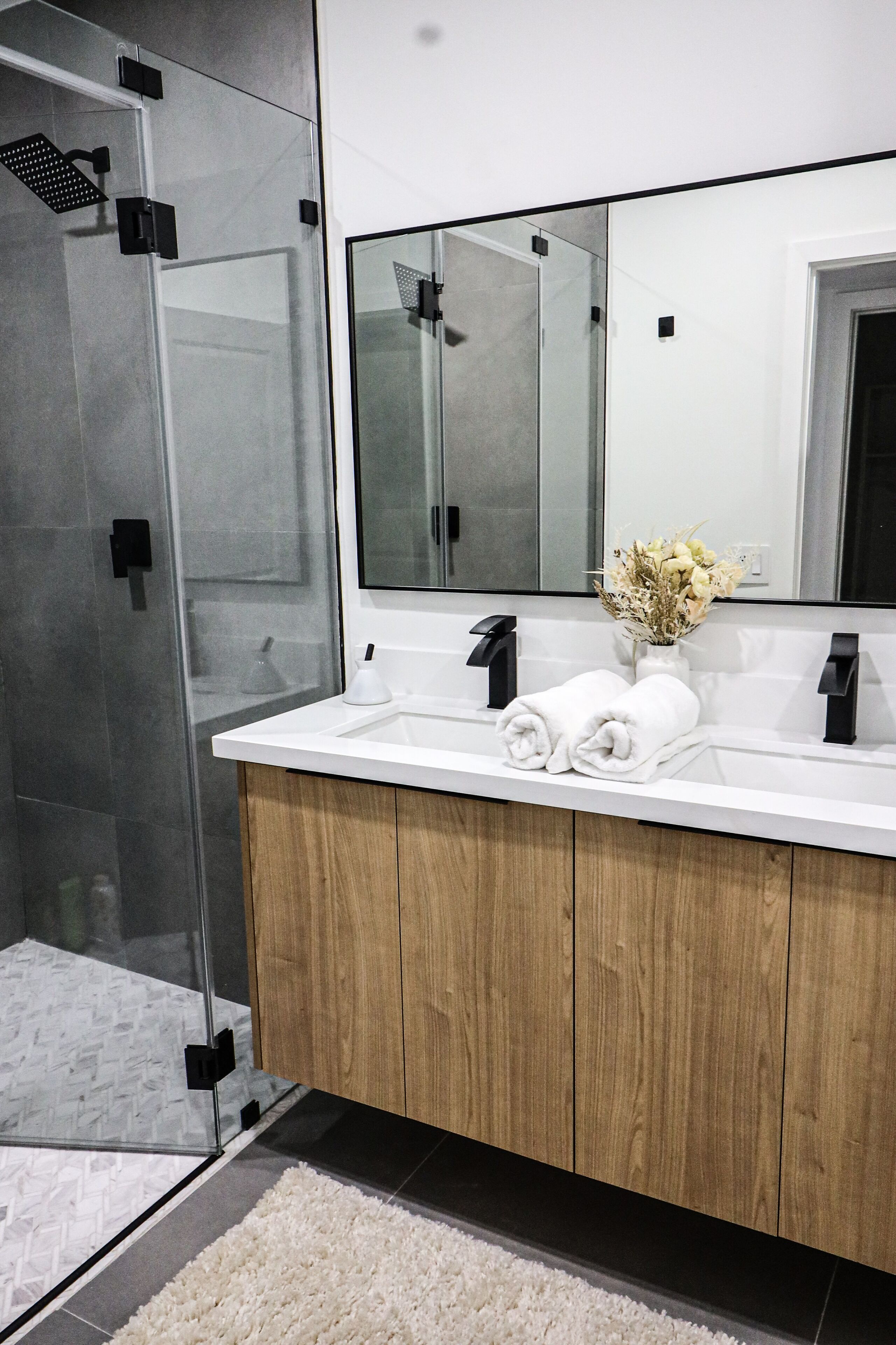 A modern bathroom with a glass shower enclosure, a white sink, wooden vanity, and a mirror above the sink.
