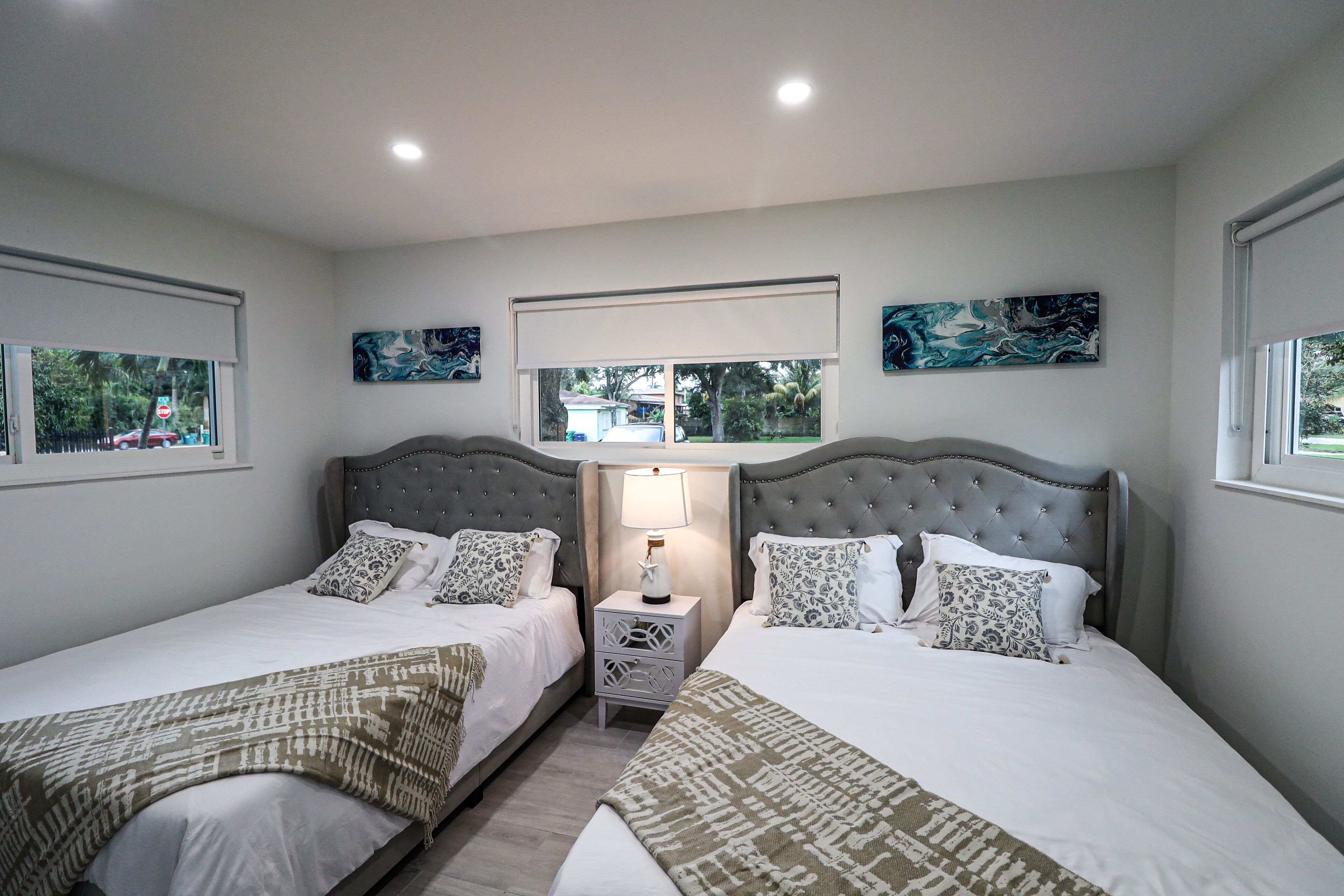 A bedroom with two beds, a nightstand with a lamp, and artwork on the walls.