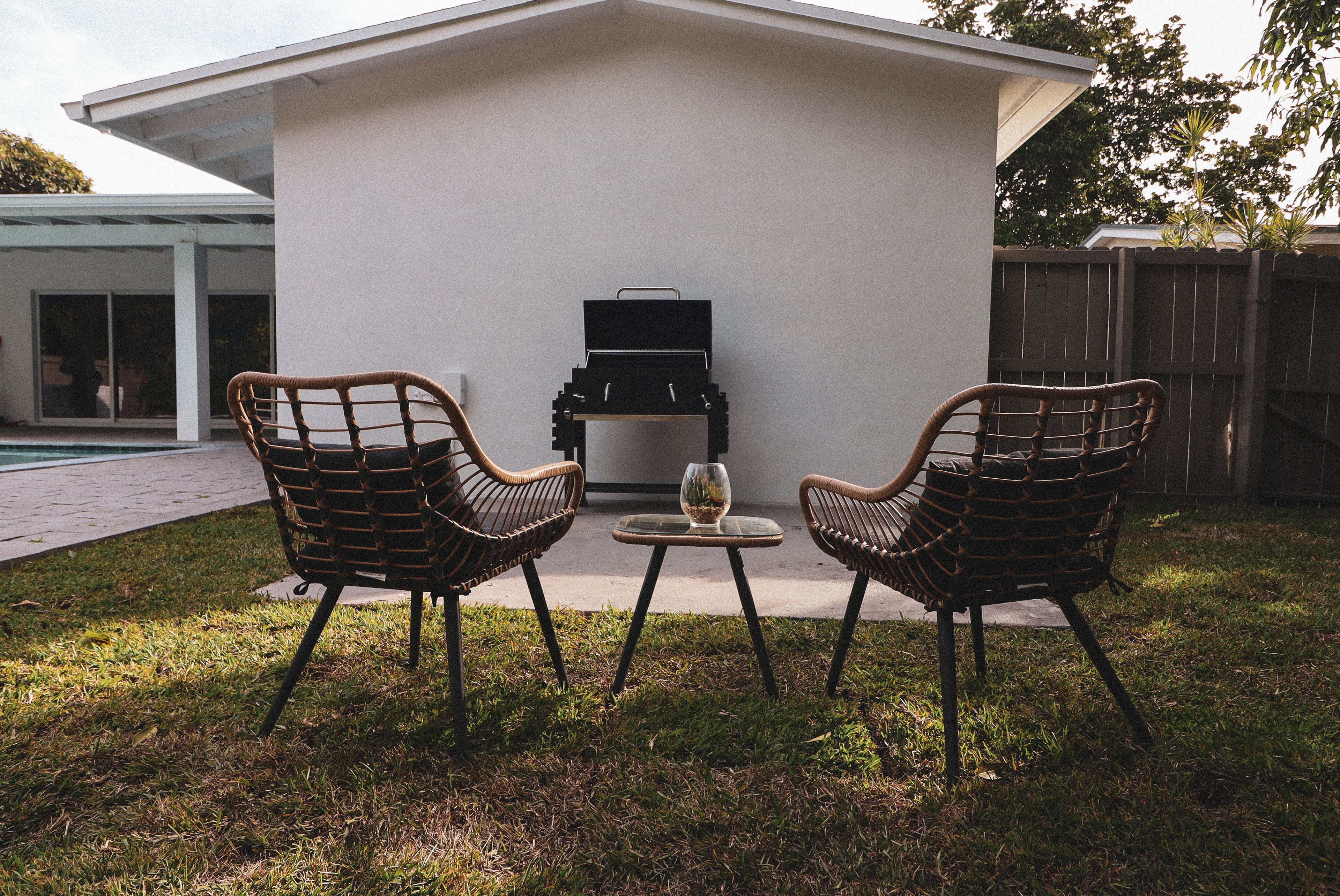 Patio esterno con due poltrone in vimini, un tavolino, un barbecue e un bicchiere di vino.