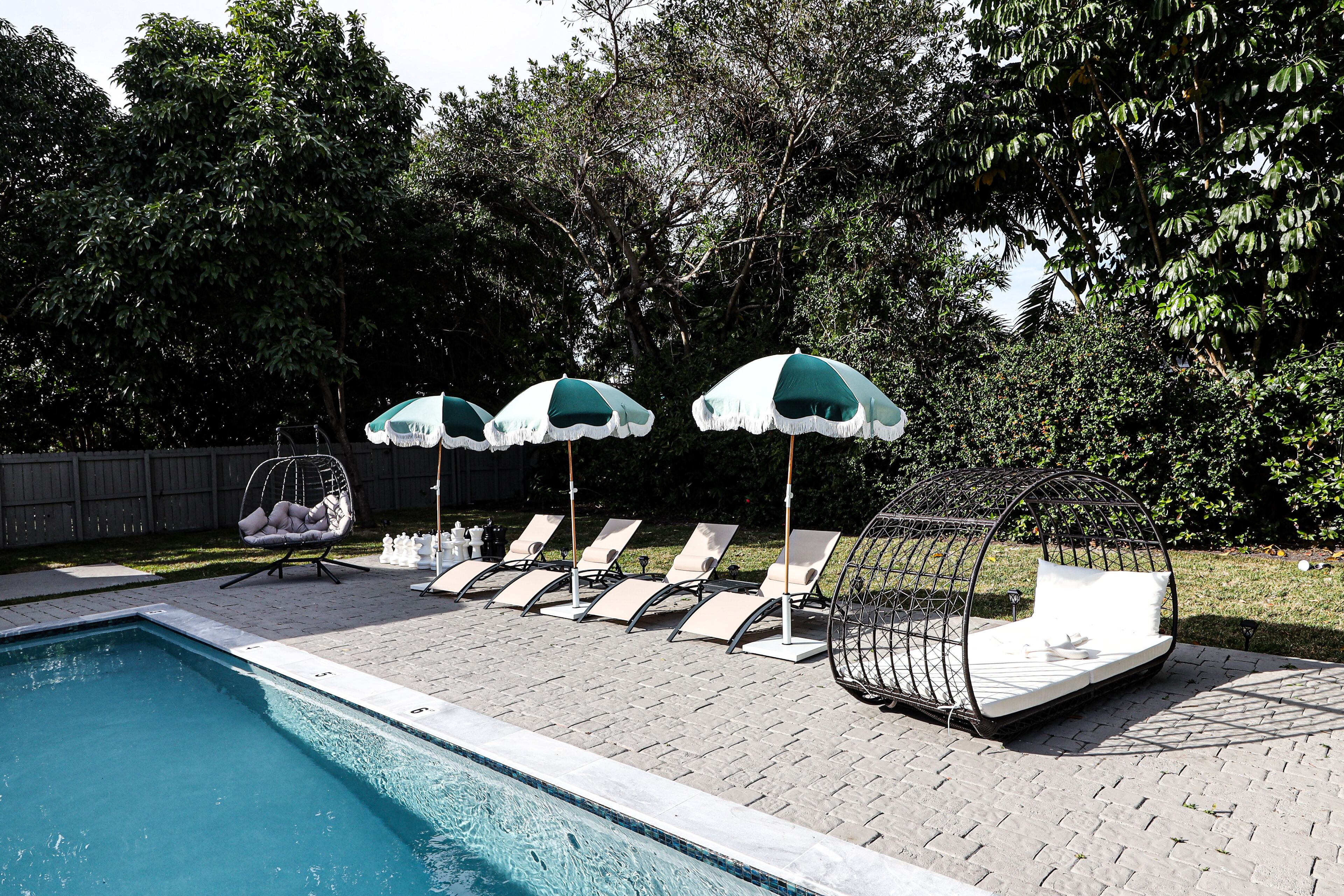 A poolside area with lounge chairs, a hanging chair, and umbrellas.