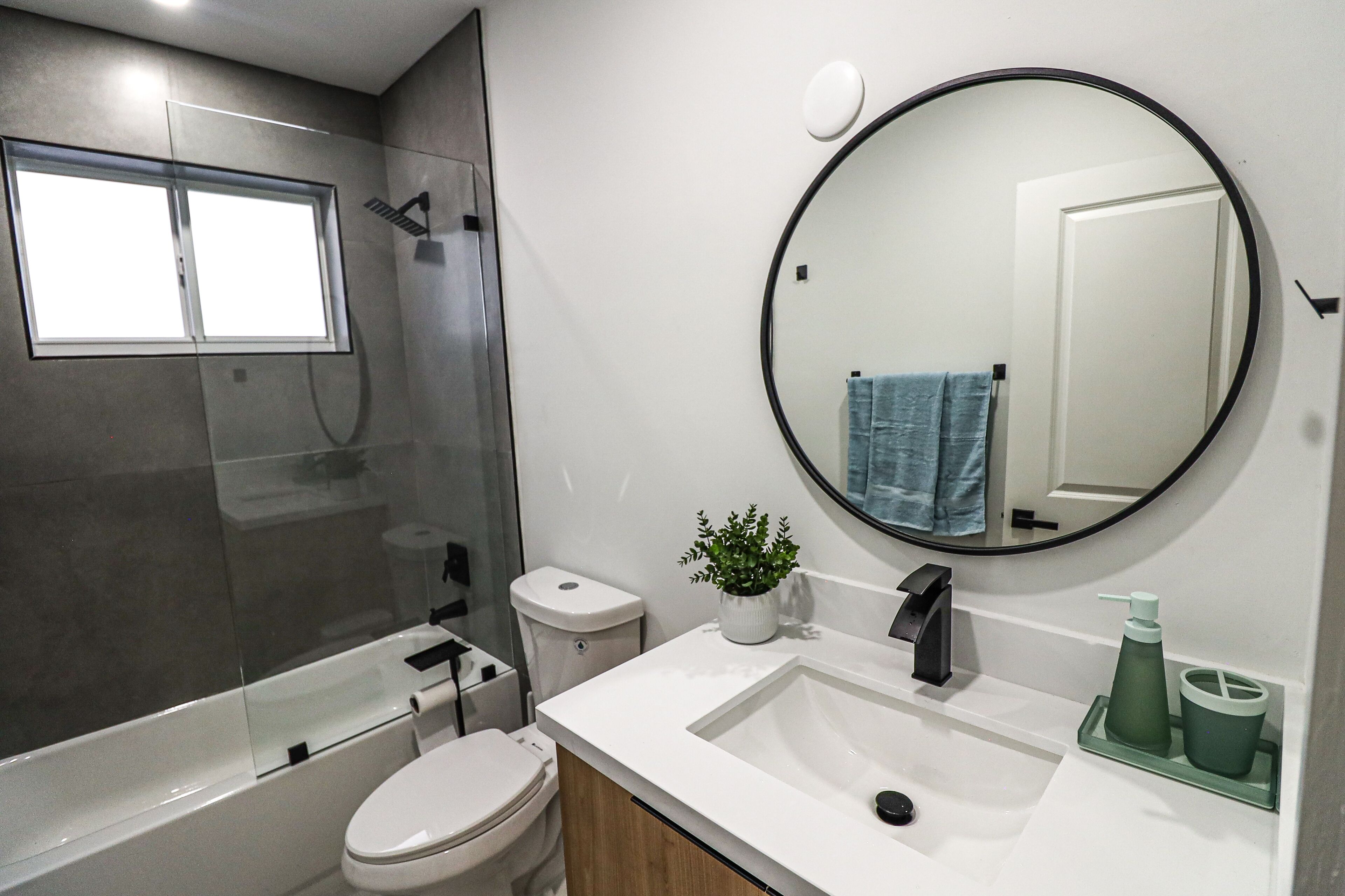 A modern bathroom with a toilet, sink, shower, and a large mirror.