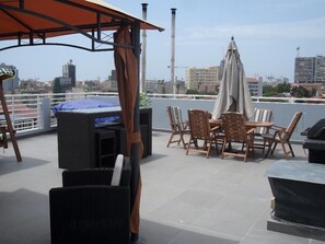 Una terraza en la azotea con una mesa y sillas, una parrilla y vistas del horizonte urbano.