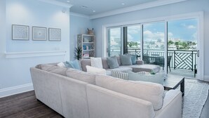 Ein geräumiges Wohnzimmer mit einer großen Couch, einem Couchtisch und einem Bücherregal. Ein Balkon bietet Blick auf die Stadt.