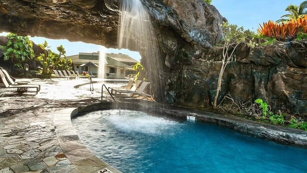 A pool area with a waterfall feature, lounge chairs, and a pool with a clear blue water.