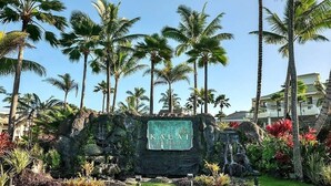 A sign for Kauai Beach Resort surrounded by lush greenery and palm trees.