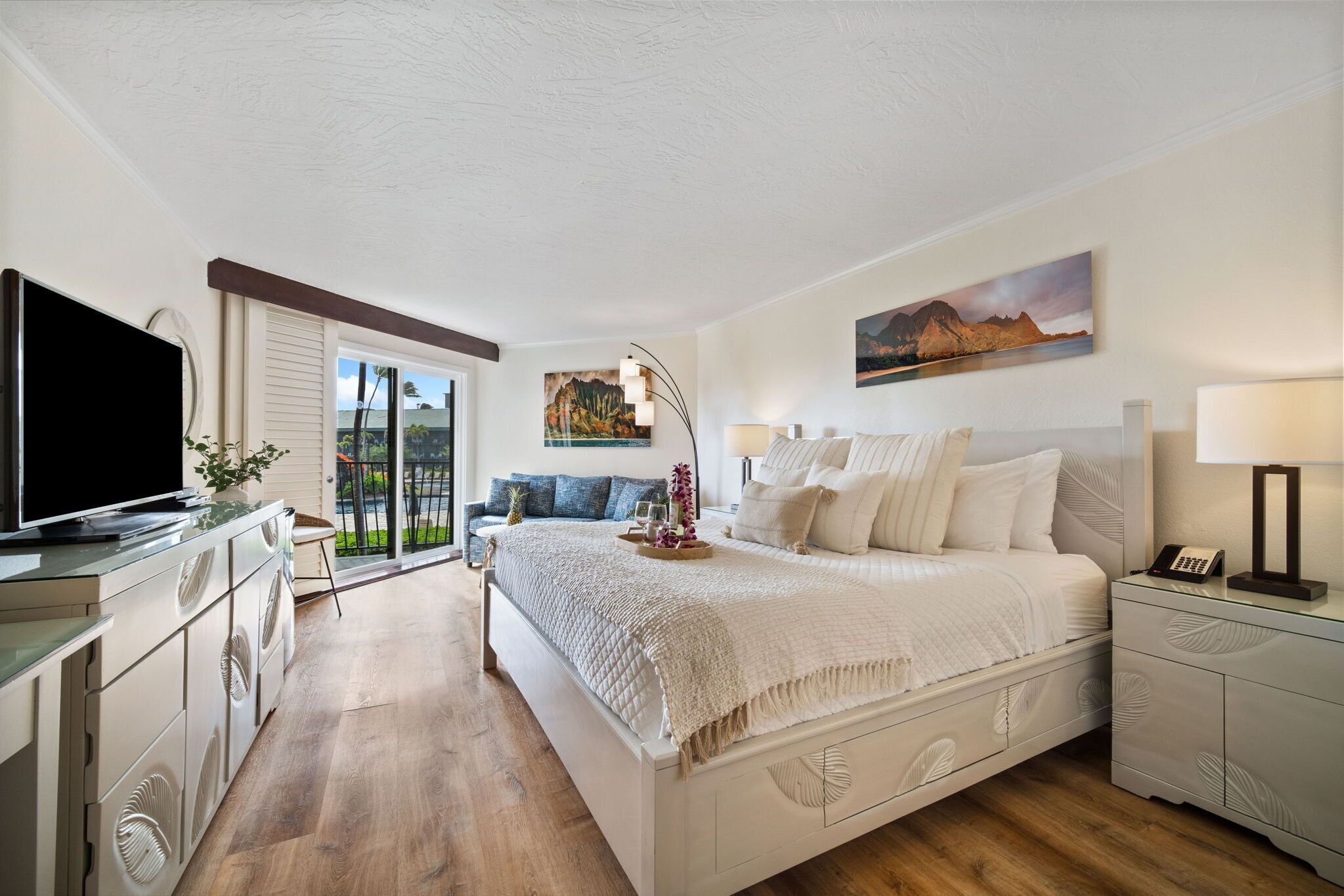 A modern bedroom with a large bed, a television, a desk with a computer, and a balcony with a view.