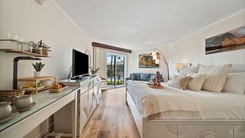 Un dormitorio moderno con cama, mesita de noche y televisor. Cuenta con un balcón que ofrece vistas al exterior.