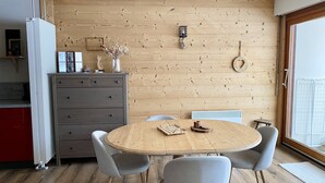 Een eethoek met een houten tafel en stoelen, een kast met lades en een houten wand met een hanglamp.