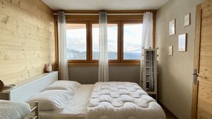 Een slaapkamer met houten inrichting, een bed met wit beddengoed, een raam met gordijnen en een deur met een deurklink.
