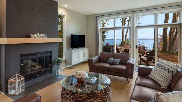 Een moderne woonkamer met een open haard, grote ramen, een televisie en comfortabele zitplaatsen.