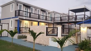 A modern two-story house with a balcony, a stone wall, and a blue pathway. - Cozy and Peacefull  (Aguadilla)