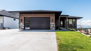 Une maison moderne à deux étages, dotée d’un grand garage, de détails en pierre et d’une pelouse bien entretenue.