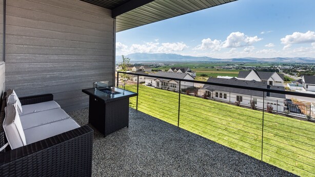 Un balcon avec un canapé en osier et une petite table, donnant sur une pelouse verdoyante et des maisons.