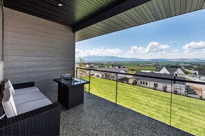 A balcony with a wicker sofa and a small table, overlooking a green lawn and houses.